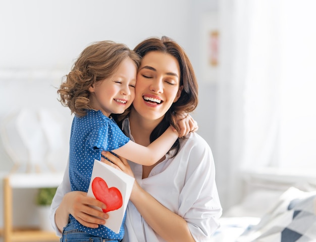 Bonne fête des mères! La petite fille félicite maman et lui donne une carte postale. Maman et fille souriante et étreignant. Vacances en famille et convivialité.