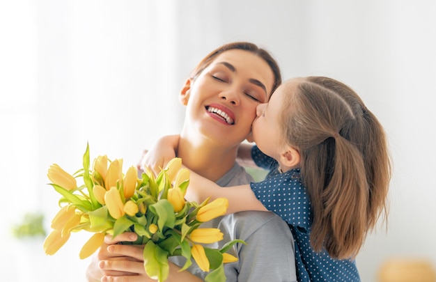 Bonne fête des mères. La petite fille félicite maman et lui donne des fleurs. Maman et fille souriante et étreignant. Vacances en famille et convivialité.