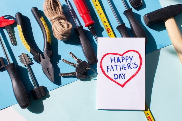 bonne fête des pères écrite à l'intérieur d'un coeur sur une carte avec des outils sur fond bleu