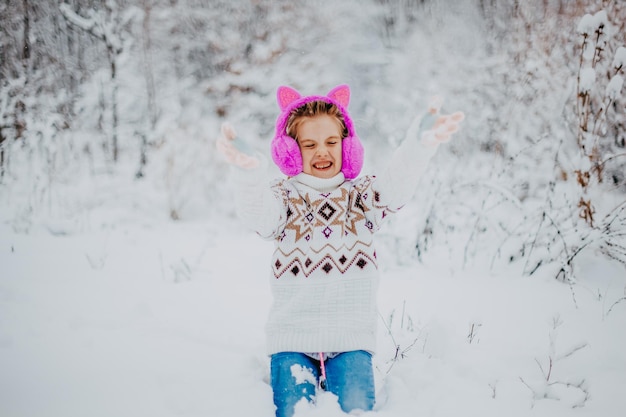 Bonne fille de bébé qui rit en pull et écouteurs s'exécutant dans un magnifique parc d'hiver enneigé le jour de noël