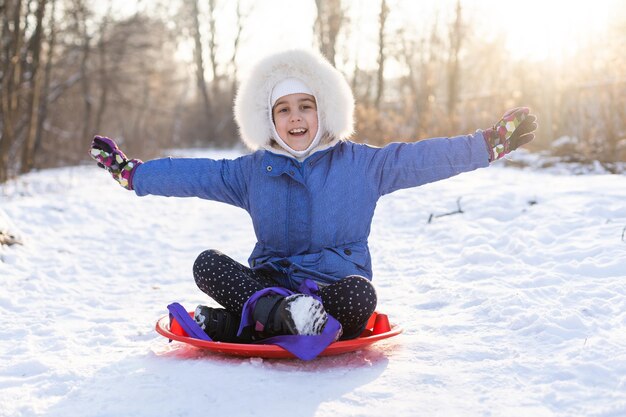 Bonne fille en hiver à l'extérieur, petite fille sur un traîneau à glace.