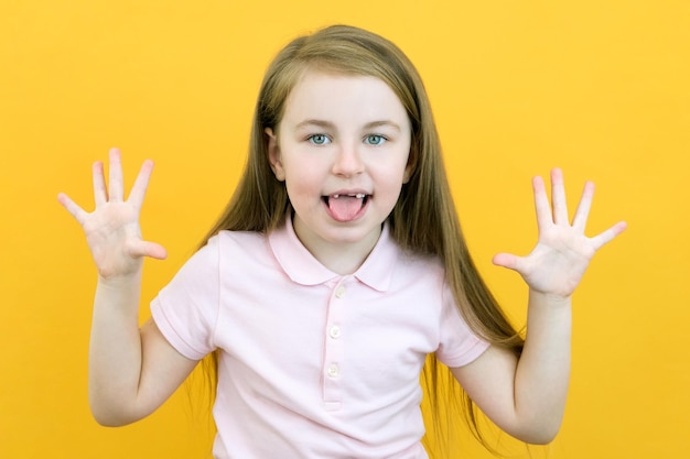 Bonne fille souriante positive montrant dix doigts tirant sa langue isolée sur fond de couleur jaune