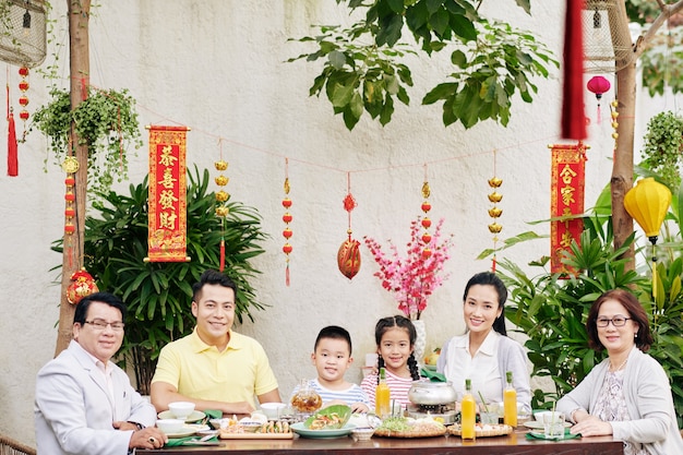 Bonne grande famille asiatique assise à une grande table à l'extérieur et célébrant le Nouvel An lunaire, décorations avec inscription de meilleurs voeux en arrière-plan