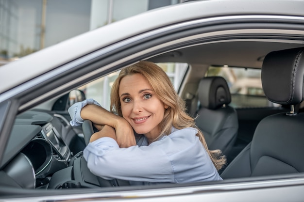 Bonne humeur. Femme blonde souriante assise dans une voiture et à la recherche de plaisir