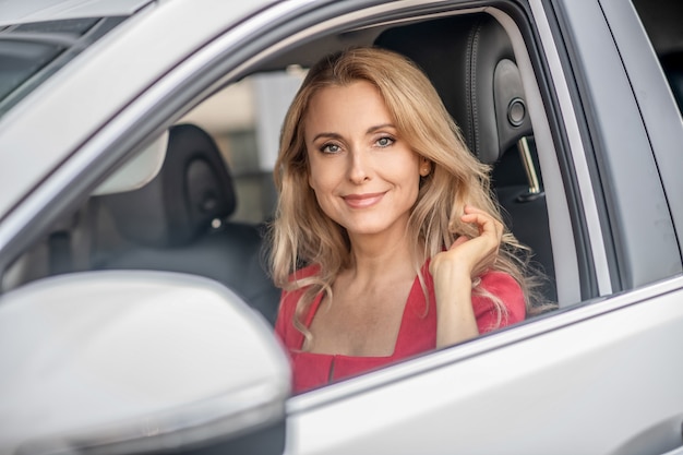 Bonne humeur. Jolie femme dans une robe rouge assise dans une voiture et à la recherche positive