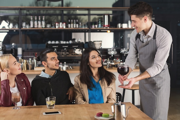 Bonne jeune entreprise d'amis buvant du café et parlant tout en étant assis dans un café moderne, espace de copie. Le serveur apporte la commande. Service, assistance, concept de style de vie