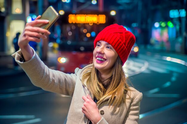 Bonne jeune femme faisant un selfie en plein air en nuit. Belle fille souriante. Belle jeune femme prenant selfie dans la ville