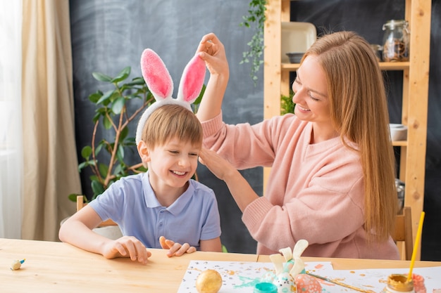 Bonne jeune mère ajustant le bandeau oreilles de lapin sur la tête de son fils pendant qu'ils s'habillent pour la fête de Pâques