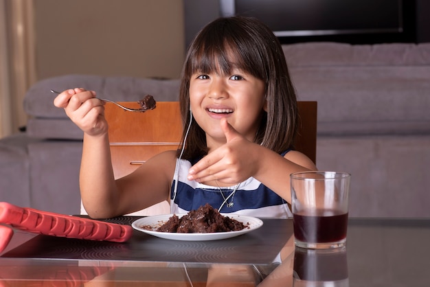 Bonne jolie petite fille regardant la tablette et manger un gâteau au chocolat