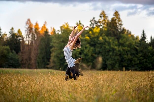 Bonne joyeuse jeune femme sautant en l'air au milieu de la prairie dorée avec de l'herbe haute. Conceptuel d'apprécier la vie, le bonheur et l'esprit de vie.