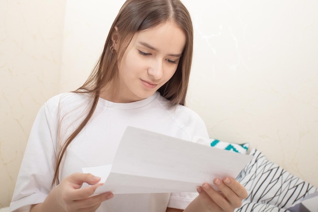 Bonne nouvelle Une fille lit une lettre sur une feuille de papier à la maison se réjouit