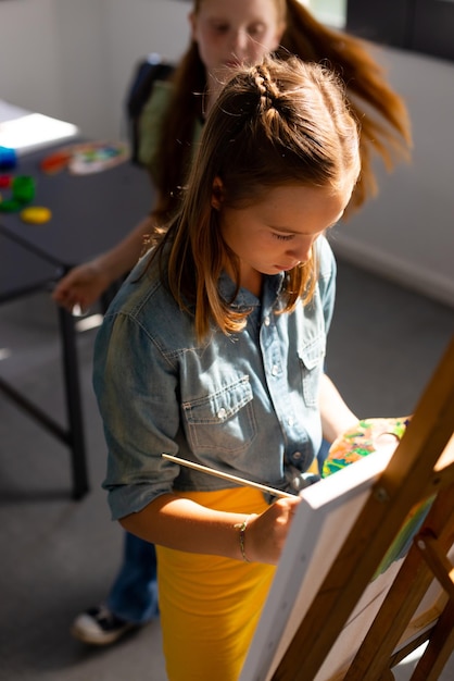 Bonne peinture d'écolière caucasienne à l'aide d'un pinceau et d'un chevalet dans la classe d'art de l'école