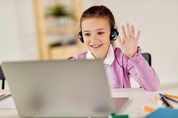 Bonne petite fille agitant tout en suivant un cours en ligne sur un ordinateur portable depuis la maison