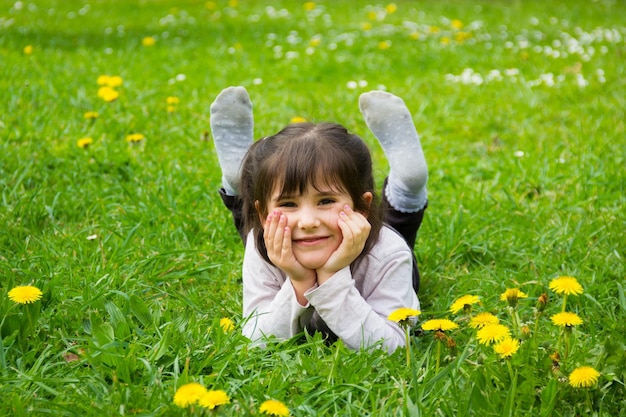 Bonne petite fille allongée sur l'herbe avec les mains tenant son visage et les pieds au parc