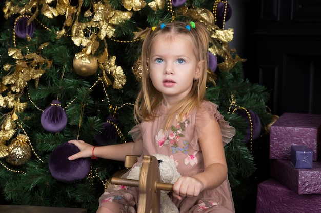 Bonne petite fille assise sur une balançoire en forme de cheval dans le décor du nouvel an