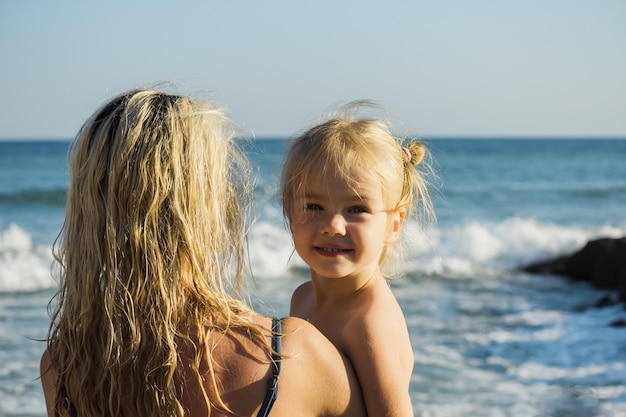 Bonne petite fille blonde dans les bras de maman sur la plage.