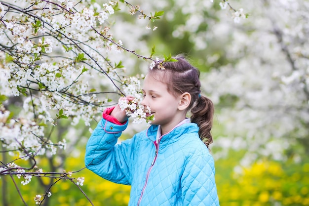 Bonne petite fille dans un jardin de printemps avec des cerisiers en fleurs