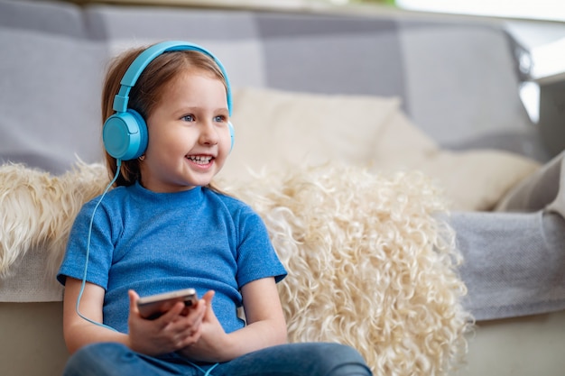 Bonne petite fille écoutant de la musique dans un casque bleu, à la maison