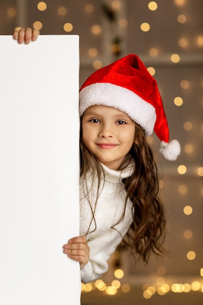 Bonne petite fille enfant en bonnet rouge tenant une bannière en carton blanc vierge avec un espace vide