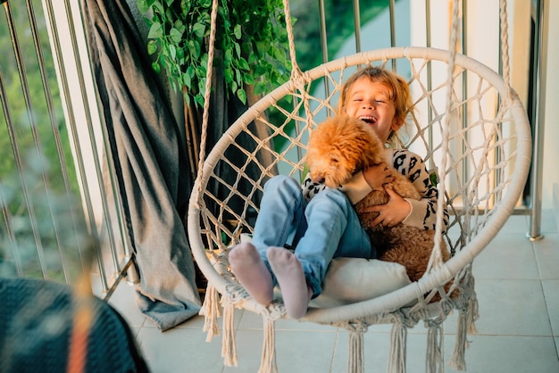 Bonne petite fille enfant étreignant avec un sourire son chien caniche à la maison sur le balcon au printemps