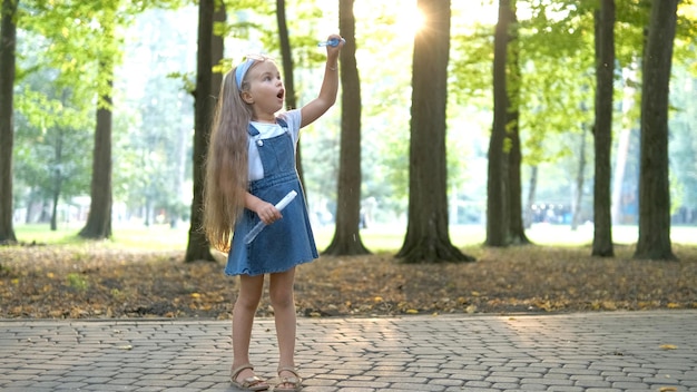 Photo bonne petite fille enfant soufflant des bulles de savon à l'extérieur dans un parc verdoyant. activités d'été en plein air pour les enfants concept.