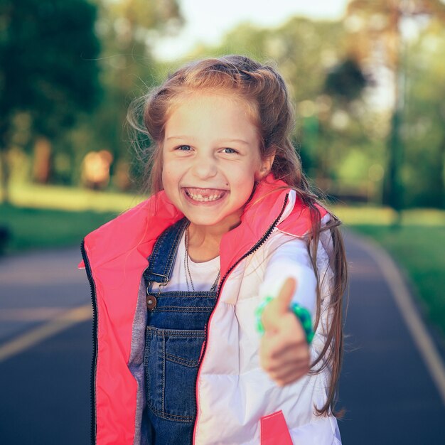 Bonne petite fille faisant le geste de pouce en l'air lors d'une promenade dans le parc au printemps