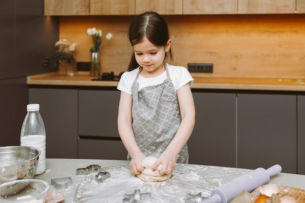 Bonne petite fille faisant de la pâte dans la cuisine un petit enfant apprend à cuisiner ou à cuire de la pâte à levure avec ses mains à la maison