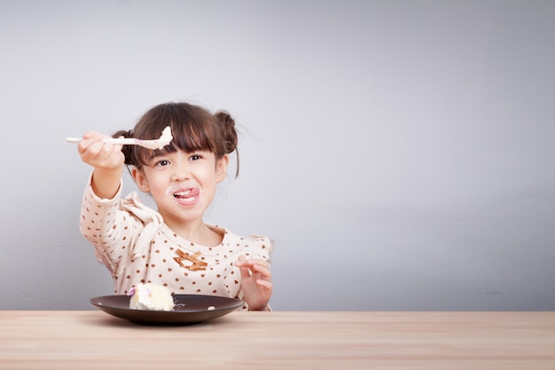 Bonne petite fille mignonne métisse profiter de manger un gâteau avec visage souriant