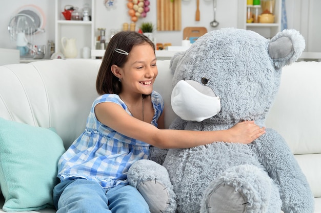 Bonne petite fille avec un ours en peluche dans un masque facial