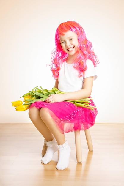 Bonne petite fille en perruque de cheveux roses avec bouquet de tulipes jaunes sur fond rose