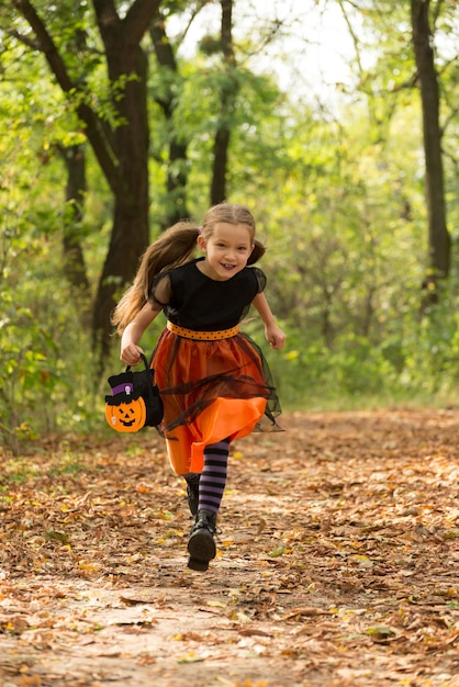 Bonne petite fille portant un costume de carnaval de sorcière et un panier de bonbons