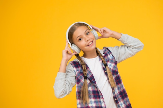 Bonne petite fille portant des écouteurs modernes Enfant mignon appréciant le son stéréo Sans fil signifie liberté Casque avec technologie sans fil Petit enfant écoutant de la musique écouteurs sans fil modernes