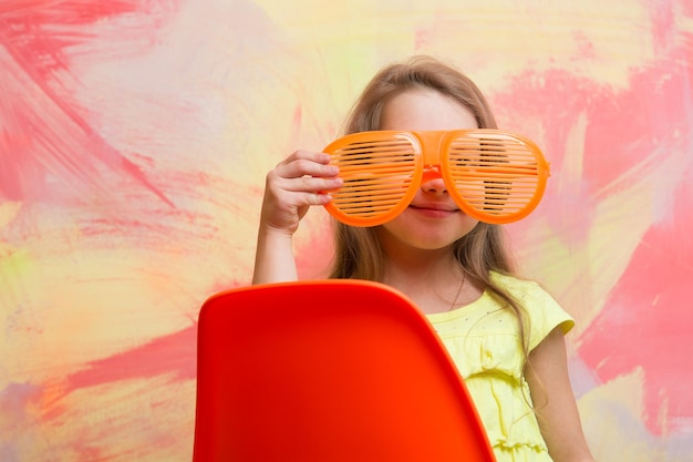 Bonne petite fille portant des lunettes assis sur une chaise sur fond coloré