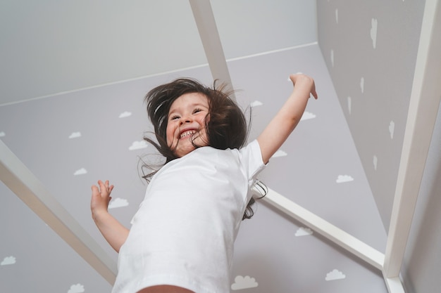 Bonne petite fille portant un pyjama blanc sautant sur le lit dans la chambre blanche. Jolie fille s'amusant tout en sautant et en jouant