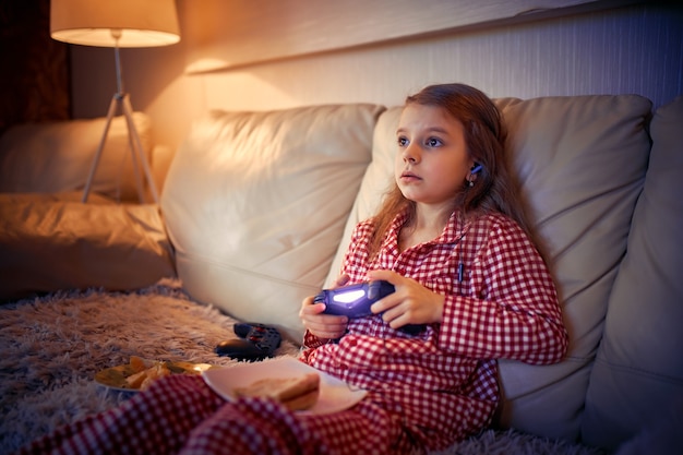 Bonne petite fille en pyjama assis sur un canapé en train de manger de la pizza