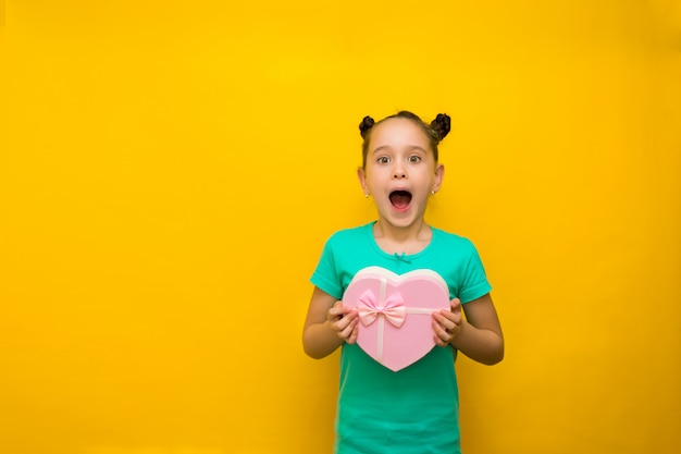 Bonne petite fille avec des queues debout isolé sur un mur jaune tenant un sac rose shopping en surprise