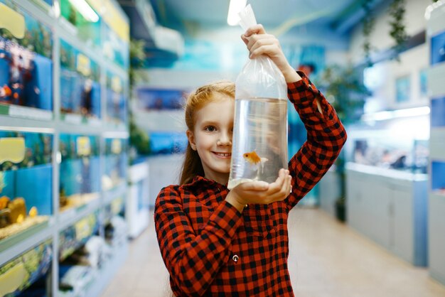 Bonne petite fille à la recherche de poissons rouges en animalerie. Enfant achetant du matériel dans une animalerie