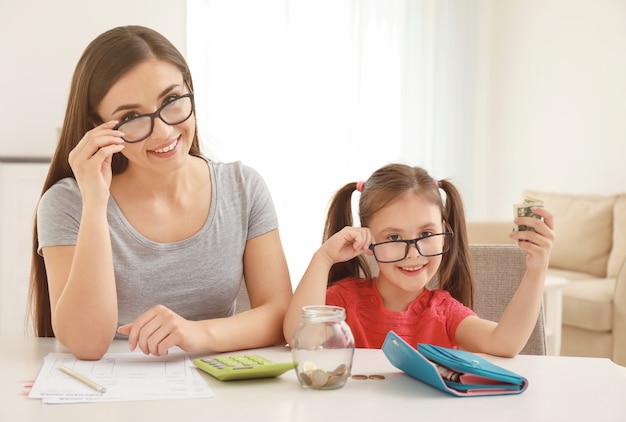 Bonne petite fille avec sa mère assise à table à l'intérieur. Concept d & # 39; économies d & # 39; argent