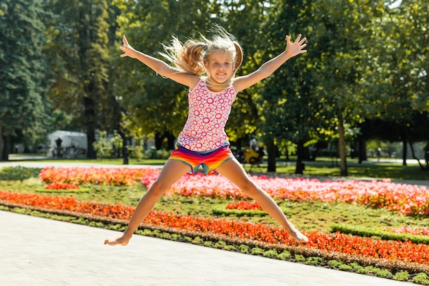 Bonne petite fille sautant dans le parc. petite fille mangeant des glaces et s'amusant dans la ville.