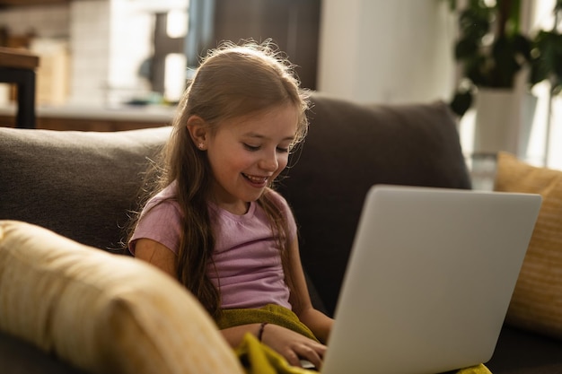 Bonne petite fille se détendre dans le salon et surfer sur le net sur un ordinateur