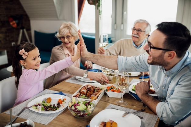 Bonne petite fille et son père s'amusant pendant le déjeuner en famille tout en se donnant un highfive à la table à manger