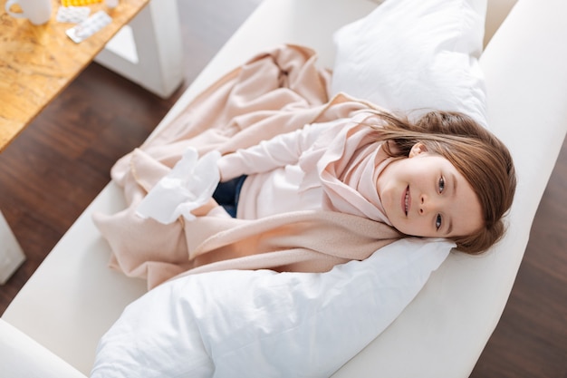 Bonne petite fille souriante assise sur le canapé et se reposer à la maison tout en se sentant mieux