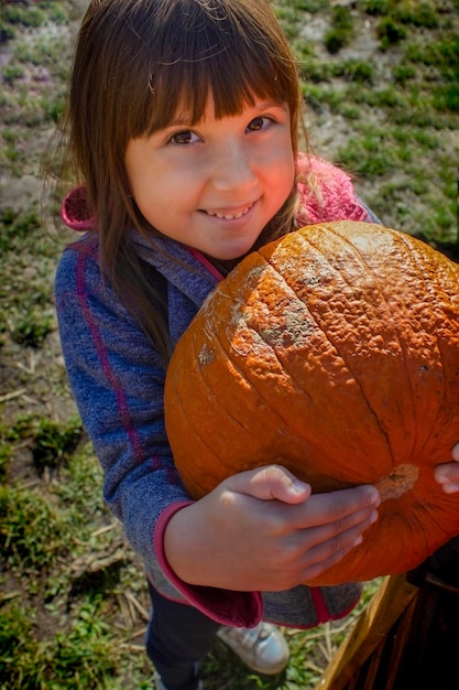 Bonne petite fille tenant une grosse citrouille se préparant pour Halloween ou Thanksgiving