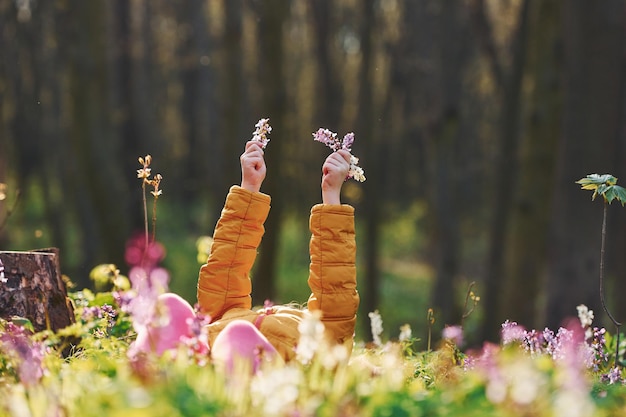 Bonne petite fille en tenue décontractée allongée sur le sol dans la forêt de printemps pendant la journée