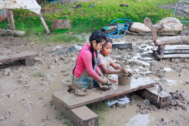 Bonne sale fille africaine et asiatique jouant dans la boue de la flaque d'eau ensemble à l'apprentissage du camp d'été en plein air