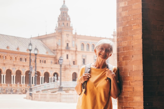 Bonne touriste senior en jaune visitant la Plaza de España à Séville Voyageur avec sac à dos