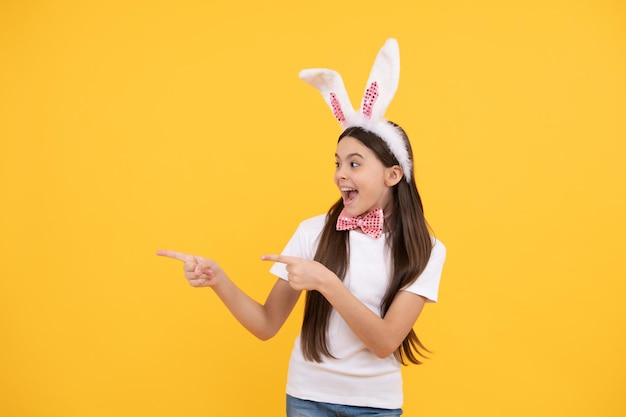 Bonne vente de pâques. bonheur d'enfance. enfant en oreilles de lapin et noeud papillon. le temps de s'amuser. adorable enfant présentant le produit. vacances de printemps pascales. espace de copie. une adolescente heureuse porte des oreilles de lapin.