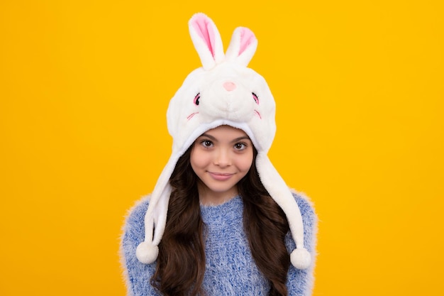 Photo bonnet d'hiver lapin belle adolescente dans un chapeau d'hiver et un pull chaud un enfant sur un fond isolé jaune heureux adolescent émotions positives et souriantes d'une adolescente