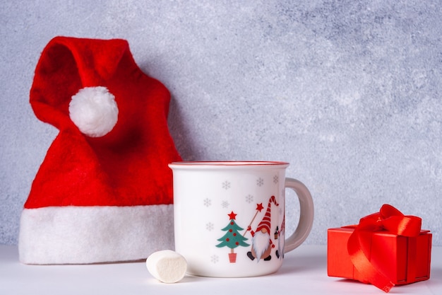 Photo bonnet de noel, mug au cacao avec des guimauves, cadeau avec ruban rouge