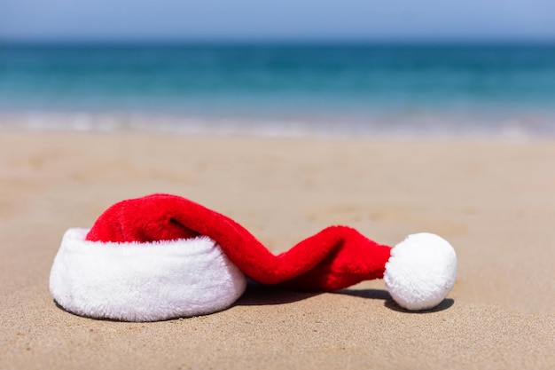 Photo bonnet de noel sur le sable en été sur le fond d'une belle mer turquoise fond de carte de noël